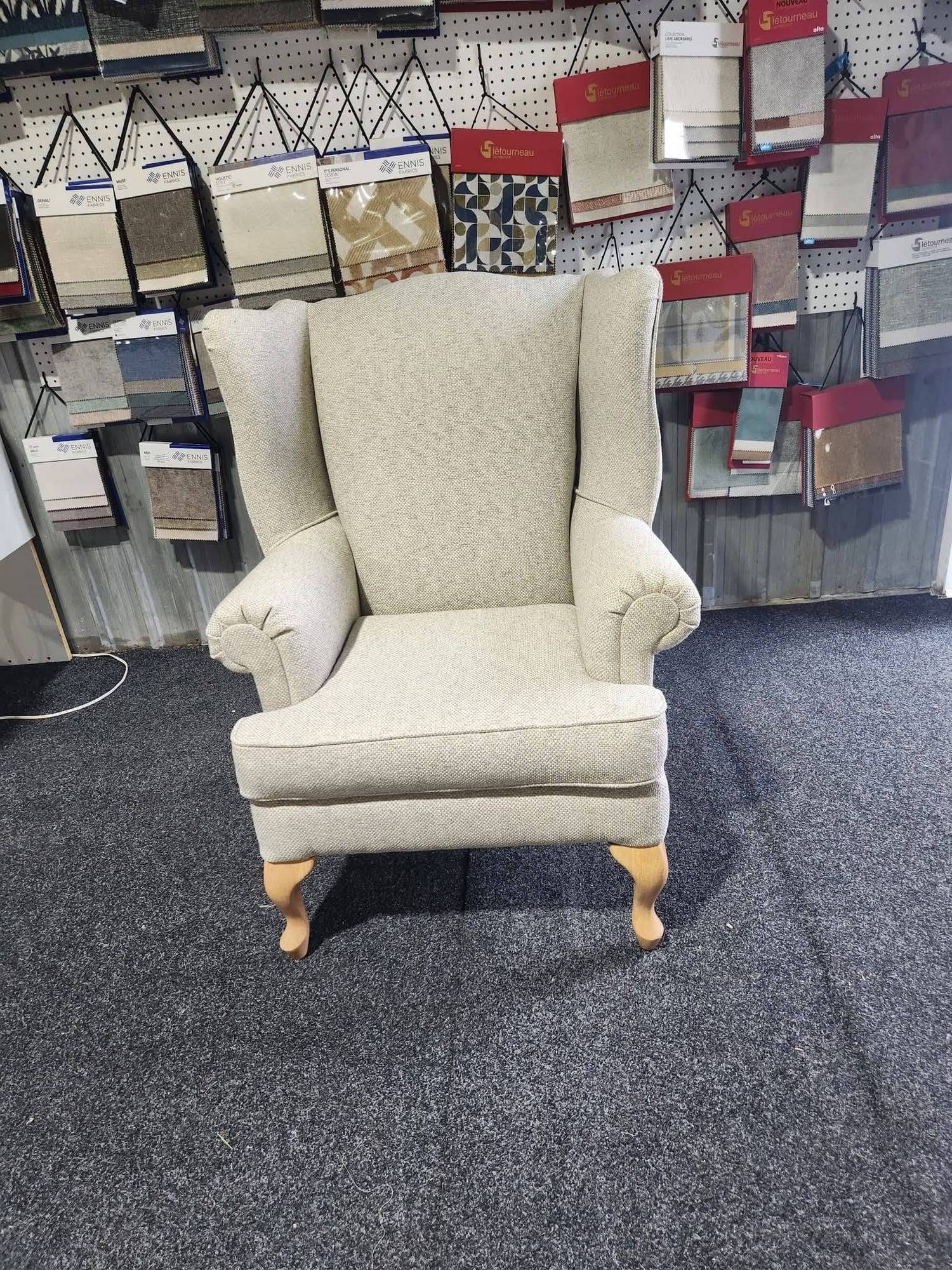 Fauteuil à oreilles aux bras roulés recouvert d'un tissu texturé beige, pieds galbés en bois