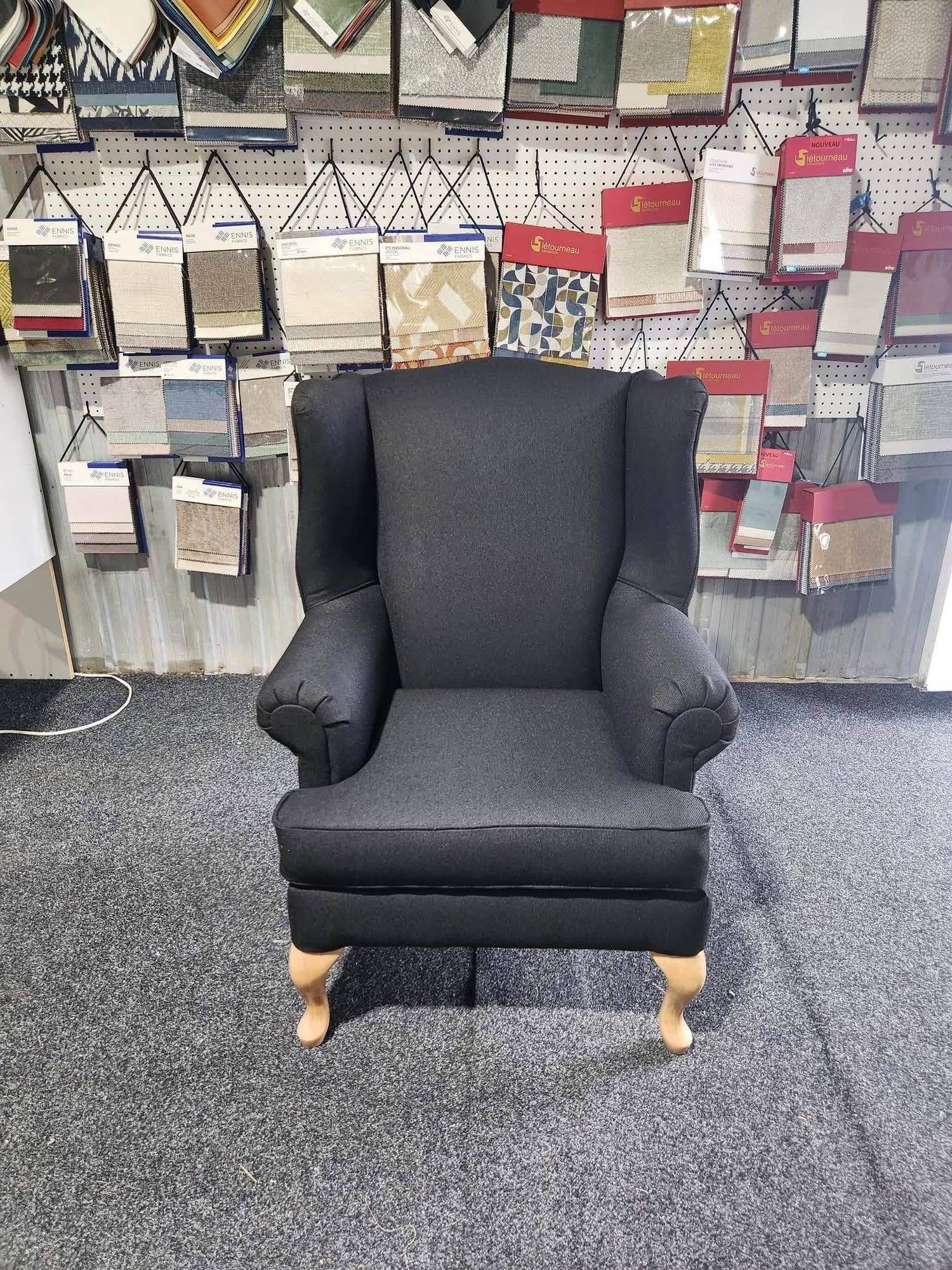 Fauteuil à oreilles recouvert d'un tissu noir, pieds galbés en bois clair