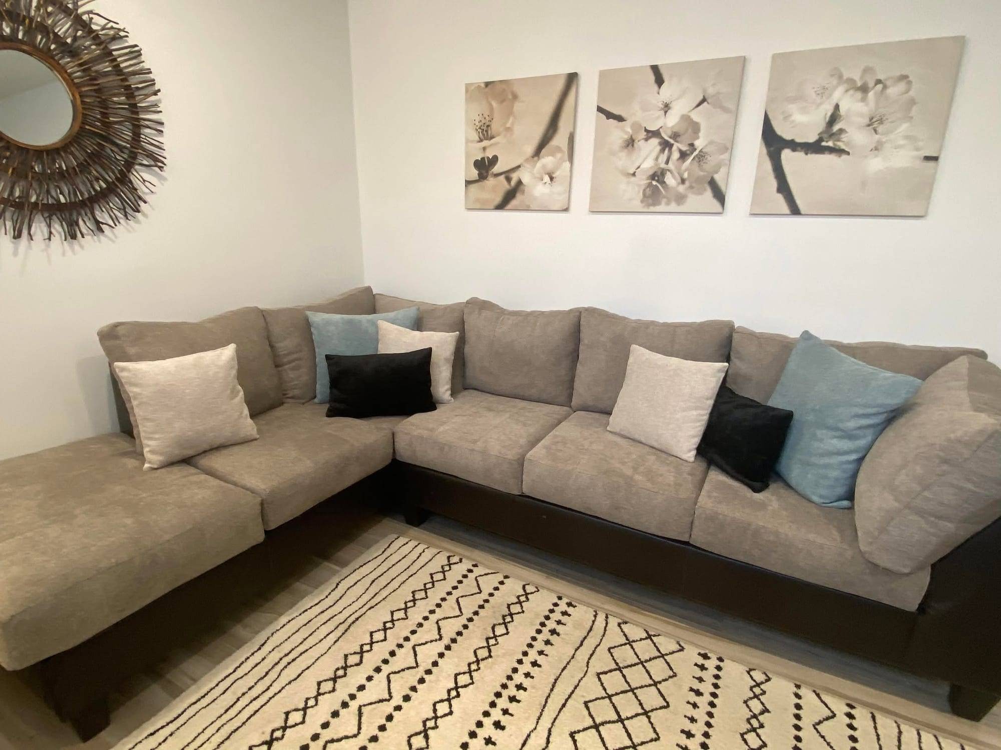 Sectionnel en L recouvert d'un tissu taupe sur base foncée, installé dans un salon