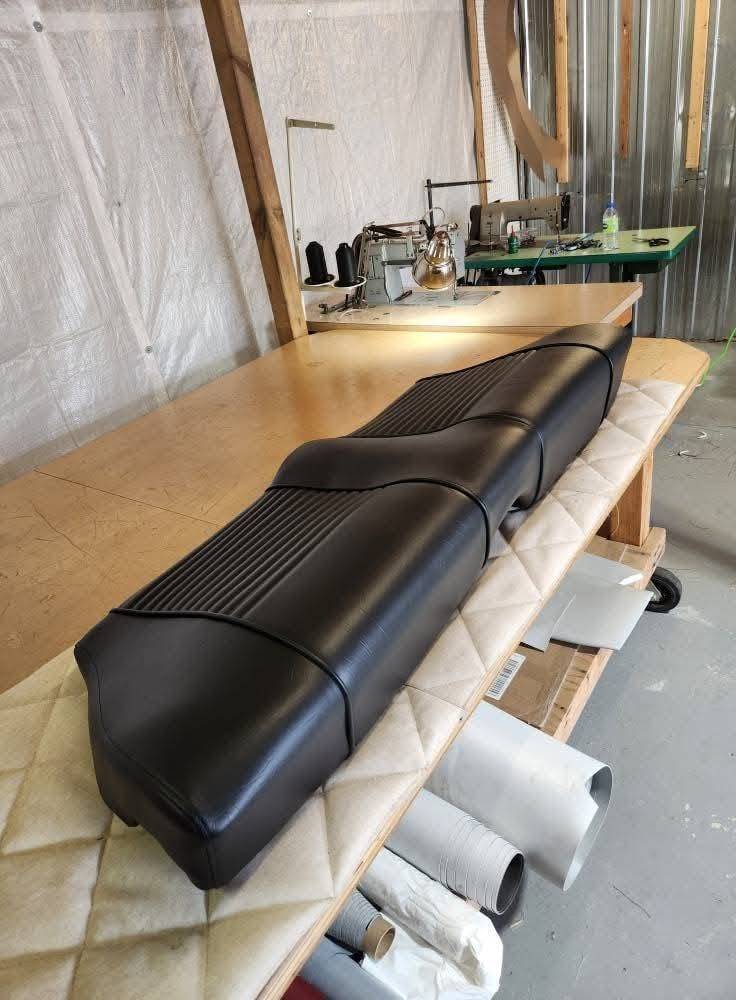 Long siège de véhicule refait en vinyle noir à plis surpiqués, sur la table de l'atelier